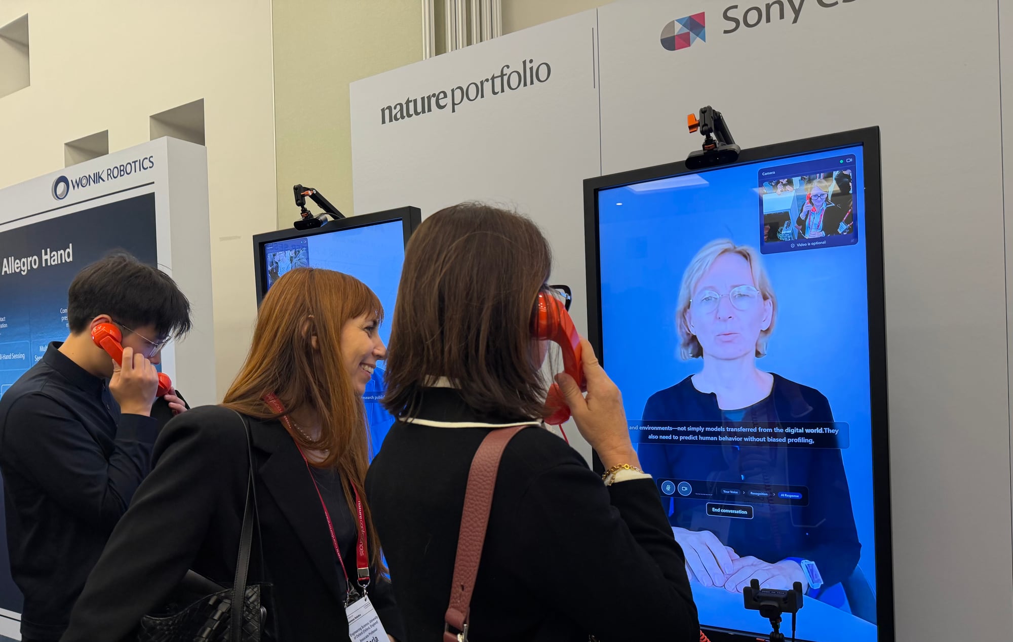 Two visitors talking with the AI Symbiont of keynote speaker Aude Billard