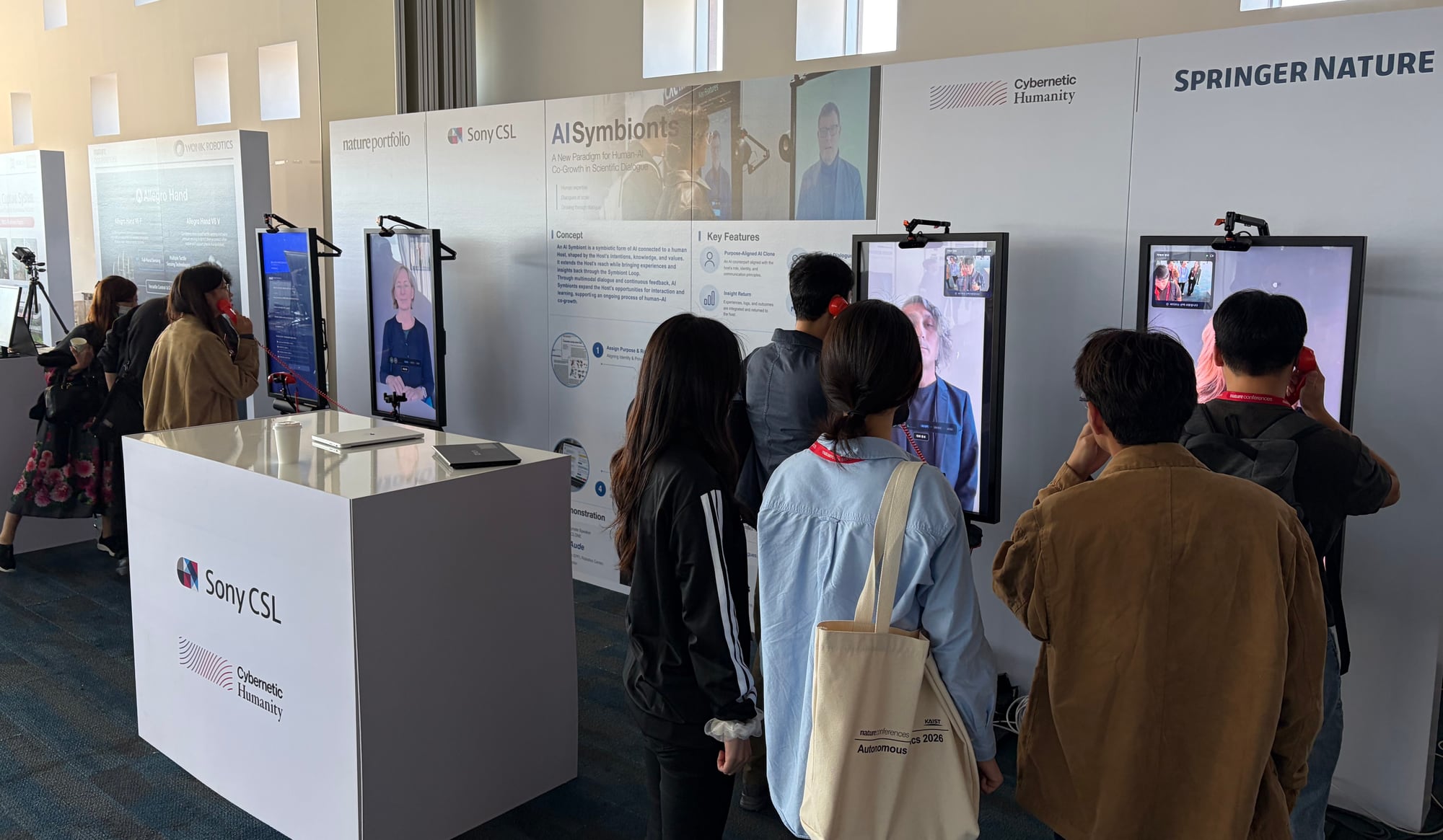 Visitors talking with AI Symbionts on red handsets at the booth